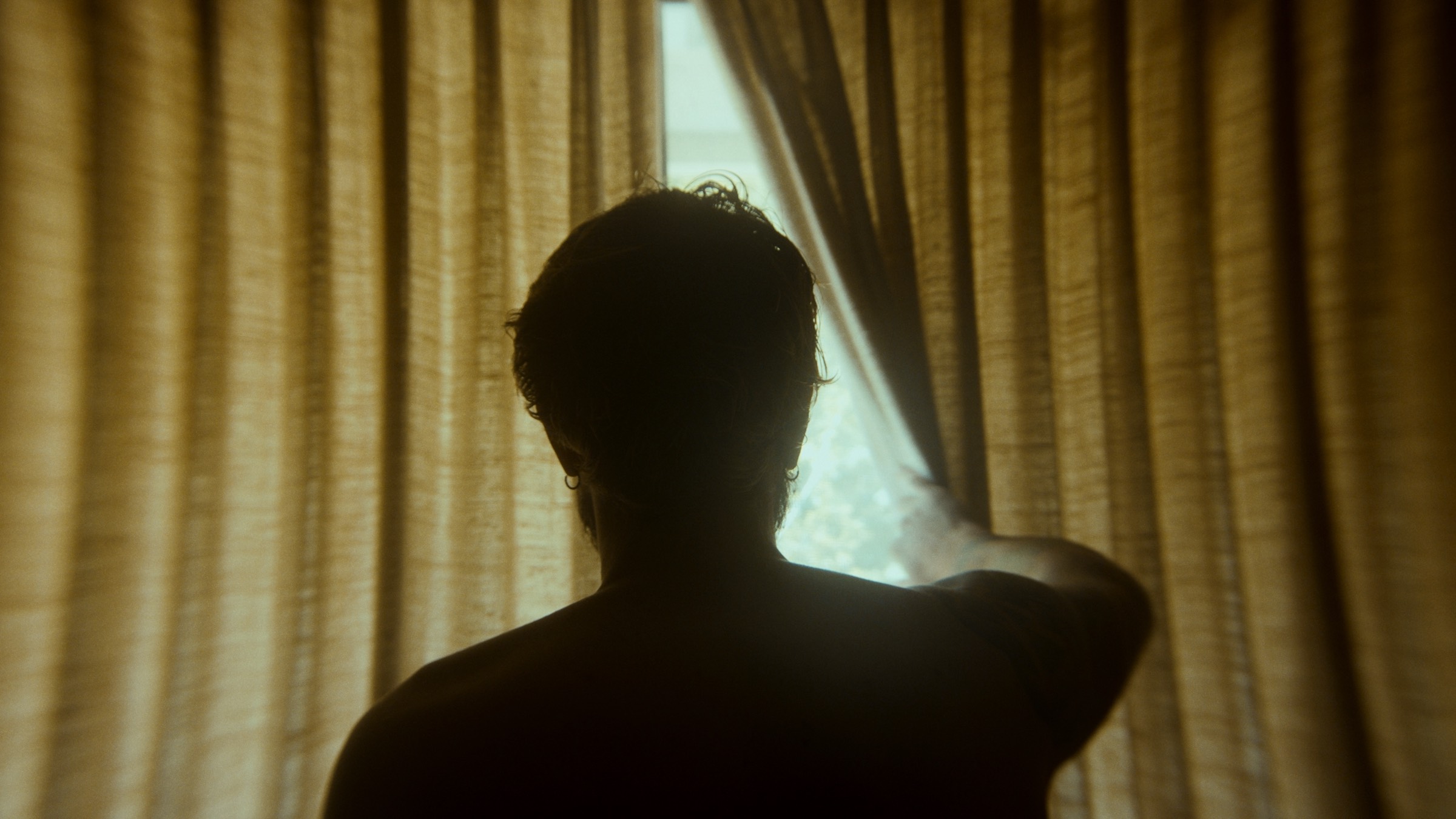 Silhouette drawing back a curtain into daylight, before