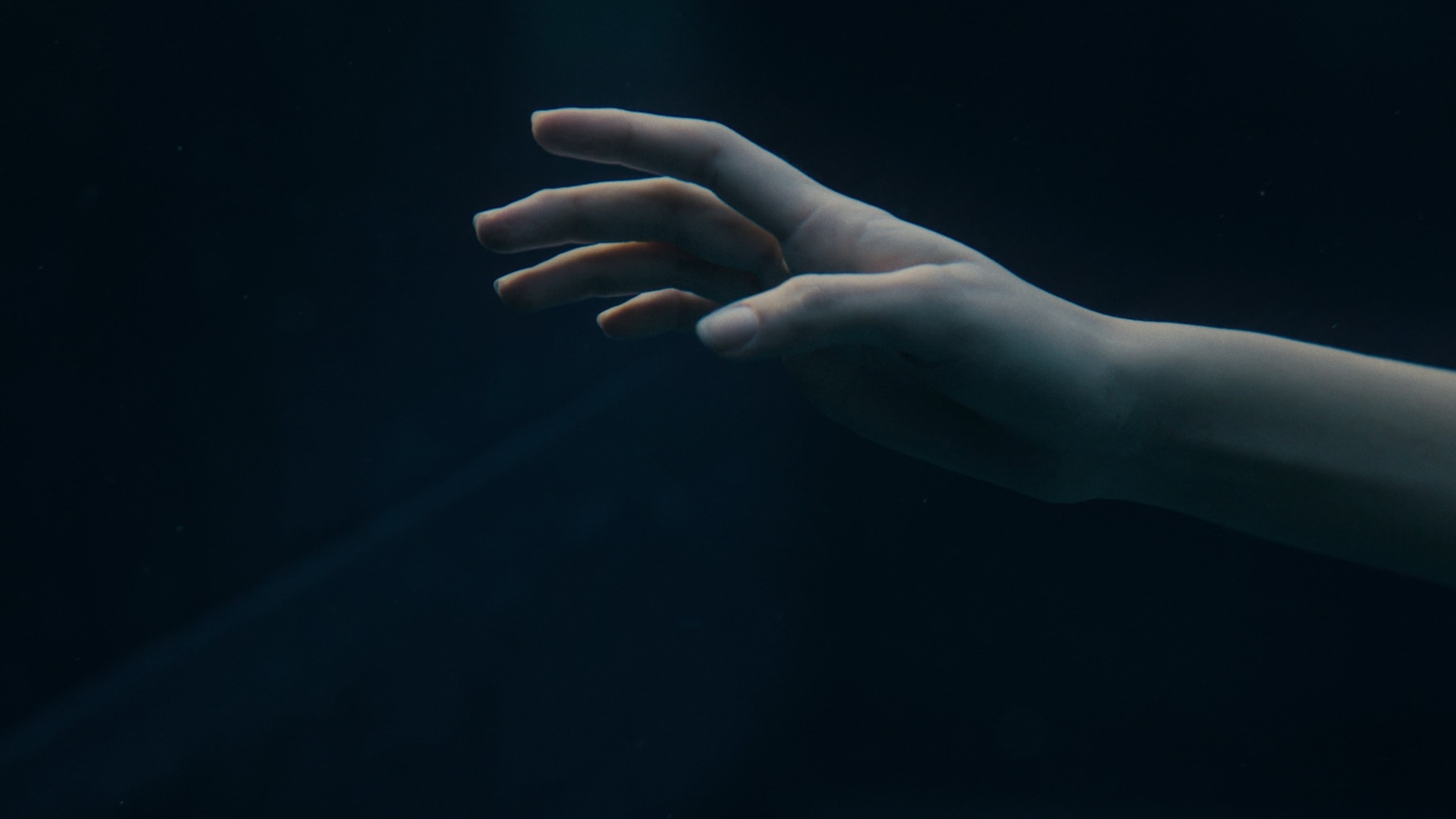 An outstretched hand underwater in near-darkness, before