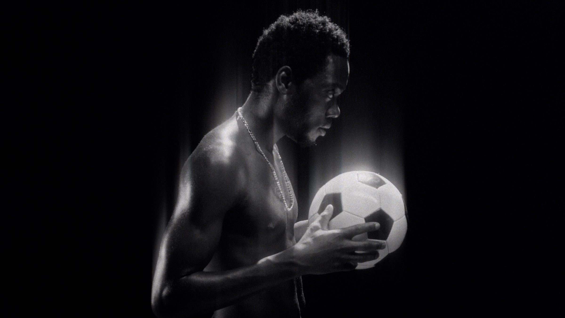 Footballer in profile holding a ball, lit against black, with ShiftBox
