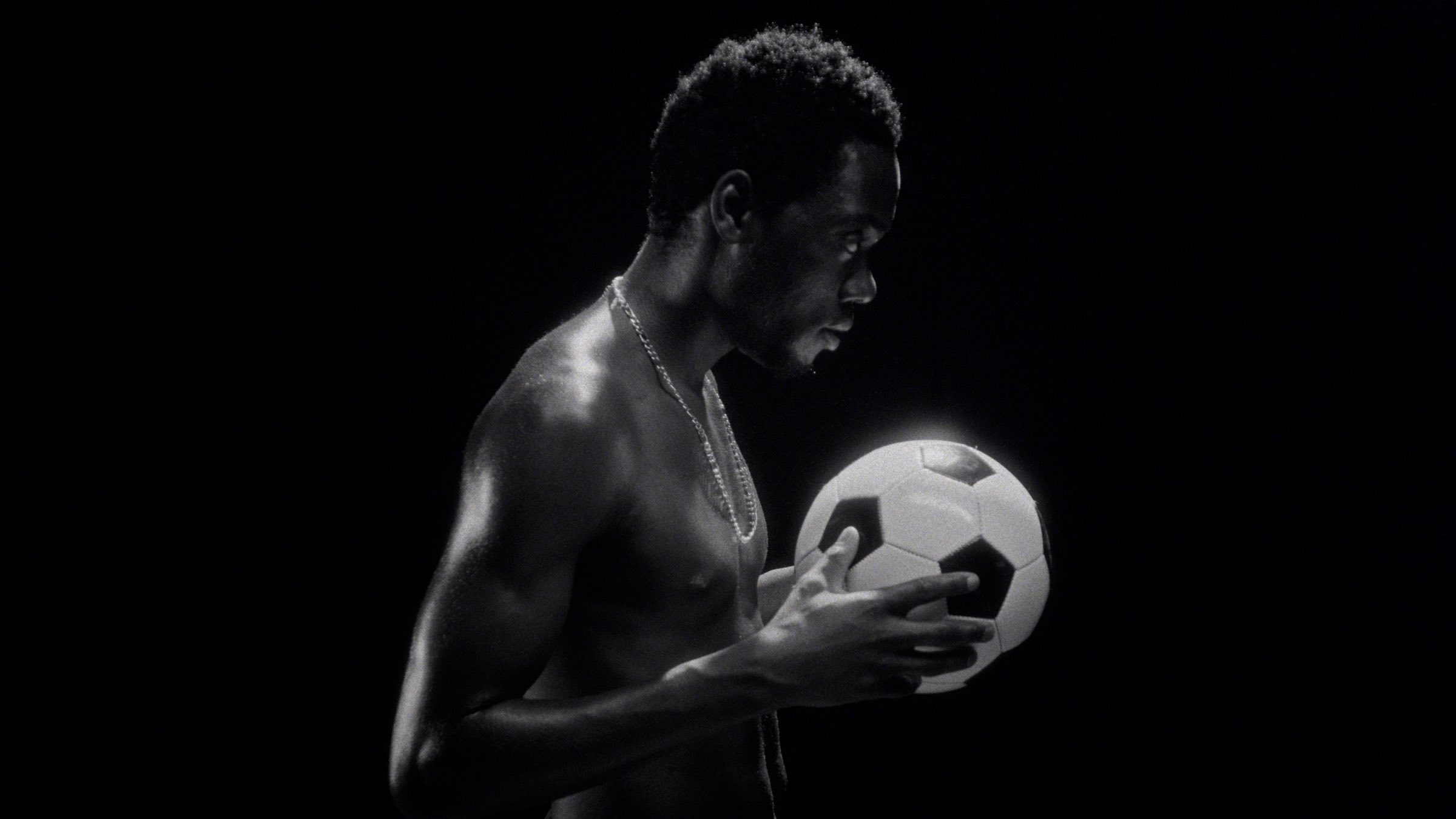 Footballer in profile holding a ball, lit against black, before